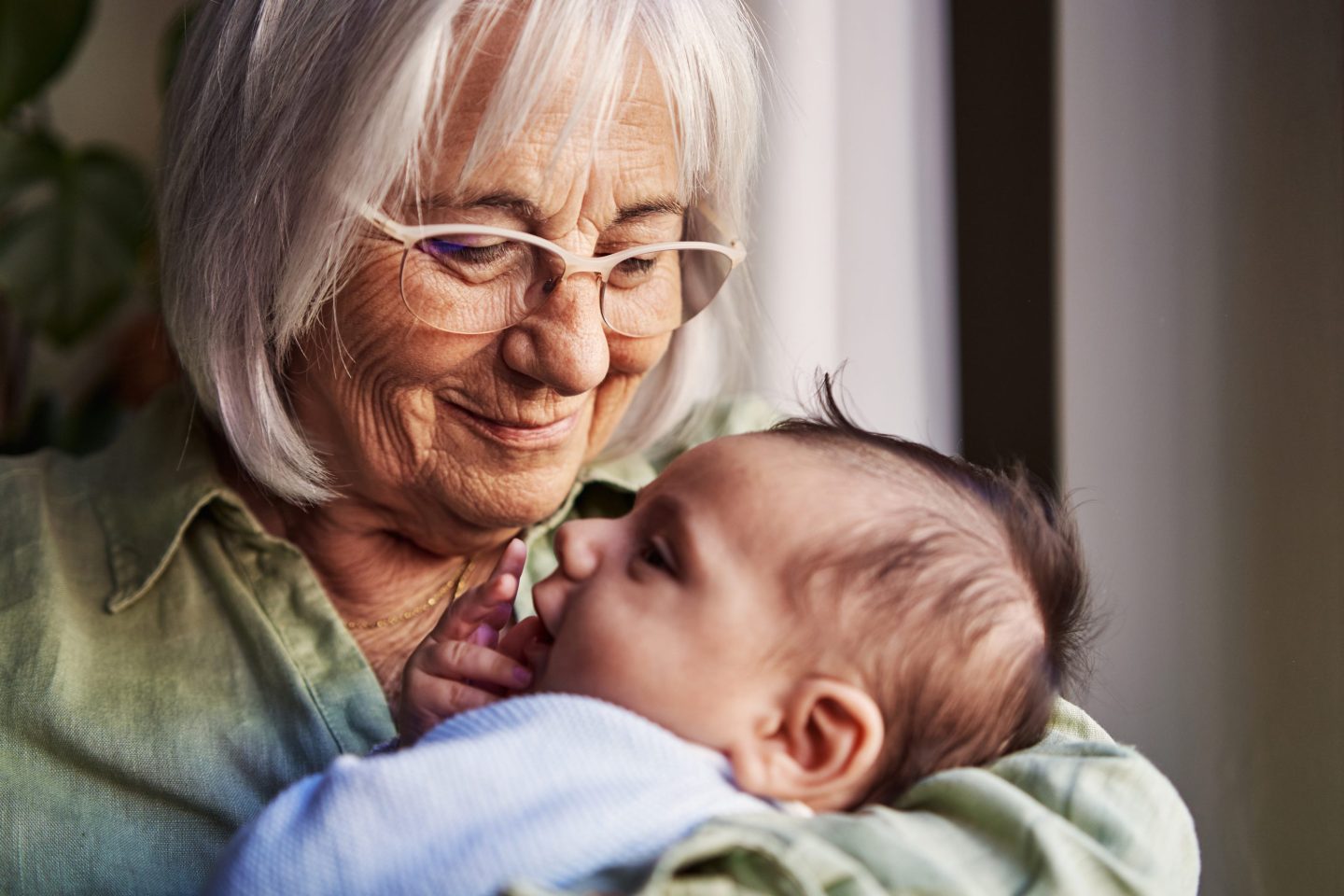 Close up portrait of a happy grandmother with gray hair holding her newborn grandchild