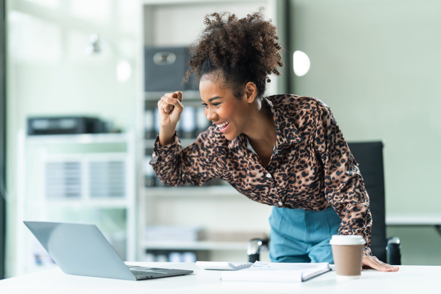 A young African American woman in a blue formal shirt with afro brown hair works as a product designer in a modern office, utilizing skills in design, CAD, CNC, and CNF.